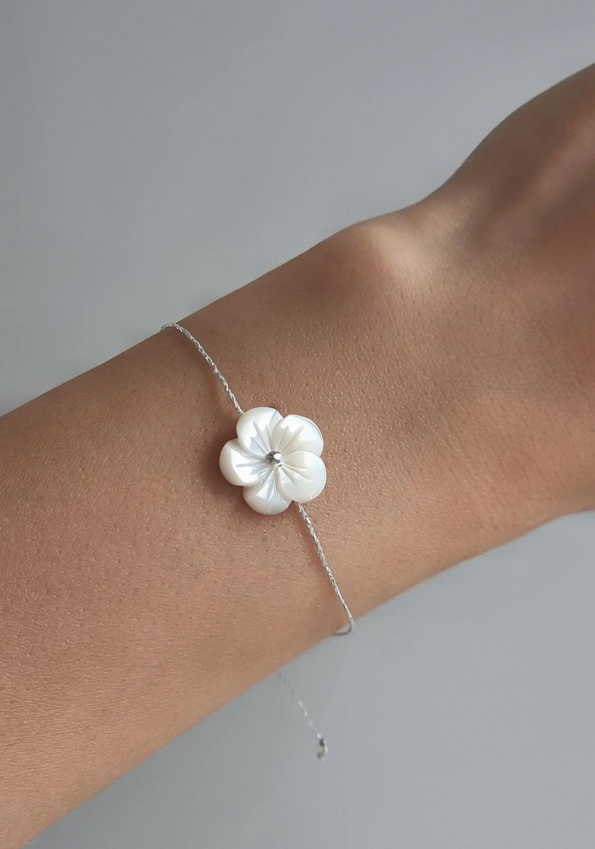 Delicate bracelet with frangipani/hibiscus mother-of-pearl flower pendant and adjustable silver-colored Linhasita thread.