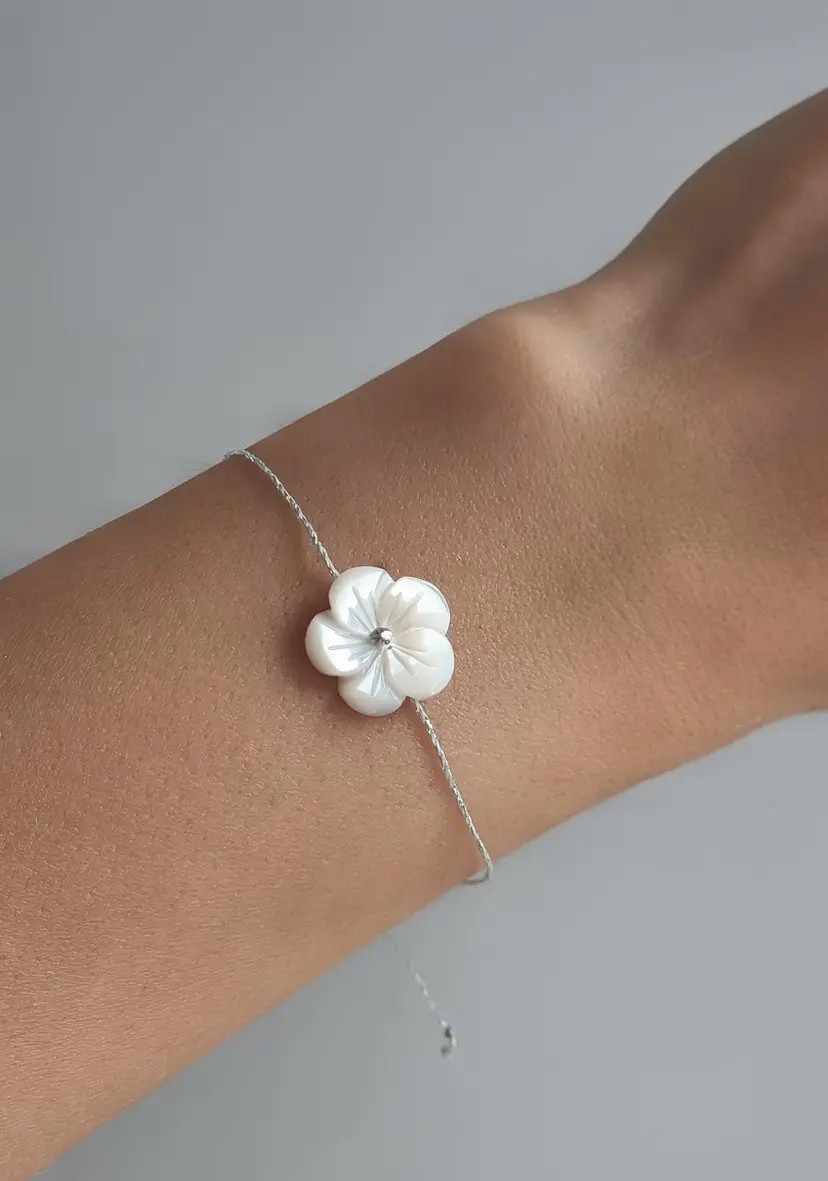 Delicate bracelet with frangipani/hibiscus mother-of-pearl flower pendant and adjustable silver-colored Linhasita thread.